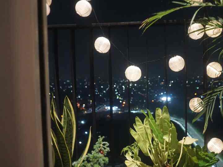 Apartment balcony at night with plants and string lights under the night sky