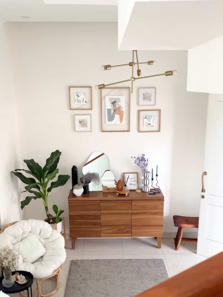 Natural tone entrance space featuring a wooden dresser, cushioned armchair, and abstract wall art in a simple interior