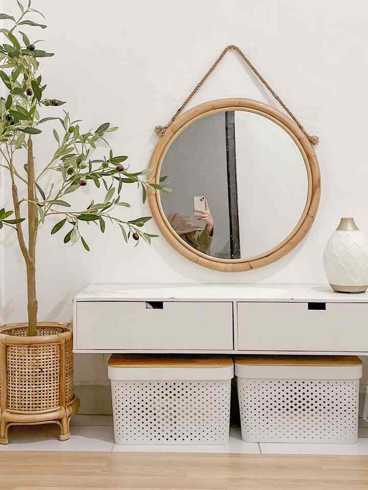 White and wood tone bedroom wall featuring a round rattan mirror and a plant in a minimal natural styled space