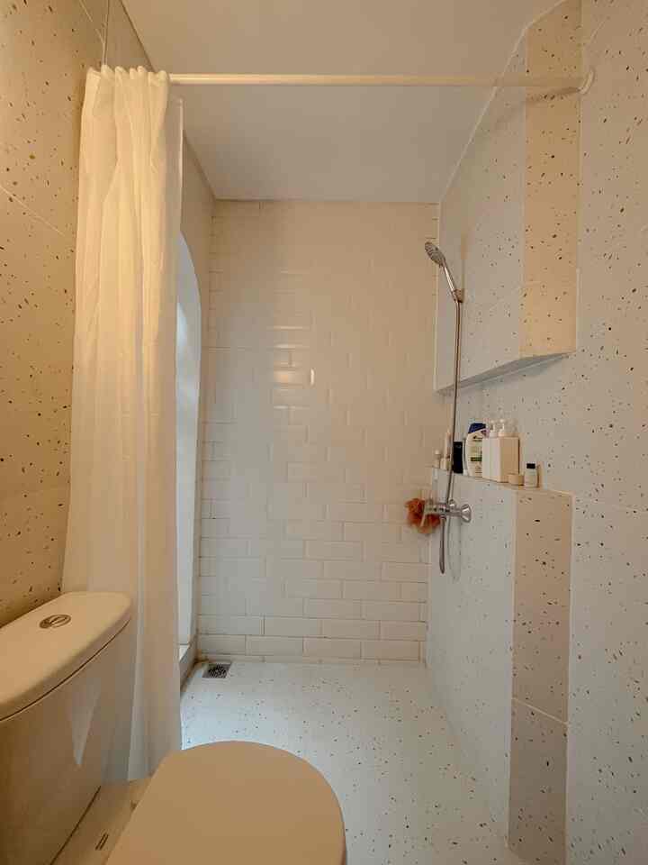 A minimalist white bathroom featuring terrazzo patterned walls and floor, an arched shower area with white curtain, creating a clean atmosphere