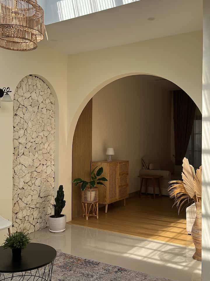 Beige and wood tone Mediterranean-Japandi style living room featuring natural wood furniture and plants in a cozy setting