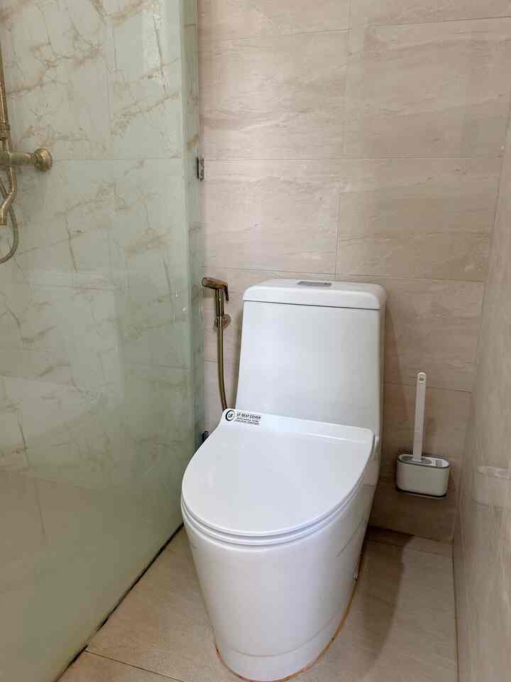 Soft beige toned bathroom featuring a white toilet and gold shower jet, creating a clean and modern atmosphere