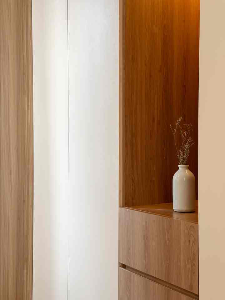 Modern walk-in closet with natural wood tones and ivory wall panel, featuring a simple white vase on wooden shelf