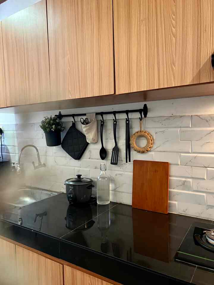 Wood tone and black combination kitchen featuring hanging utensils and electric rice cooker on a sleek countertop
