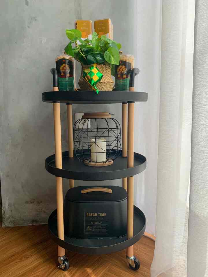 Black and wood-tone three-tier kitchen cart holding food items and decor, creating a cozy storage space