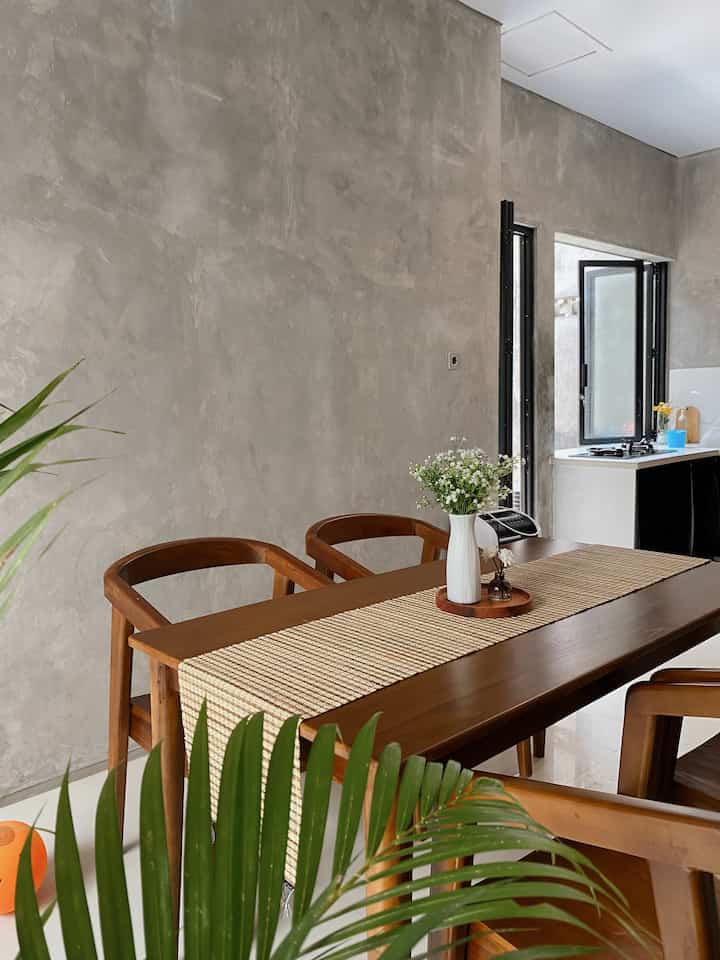 Compact dining room with natural wood tones and gray walls, featuring a wooden dining table and chairs with plants and floral decor in a modern setting