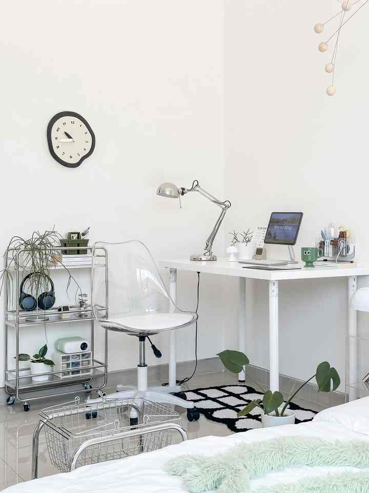 Minimalist home office in white and silver tones featuring a clean white desk and transparent chair, creating a functional workspace