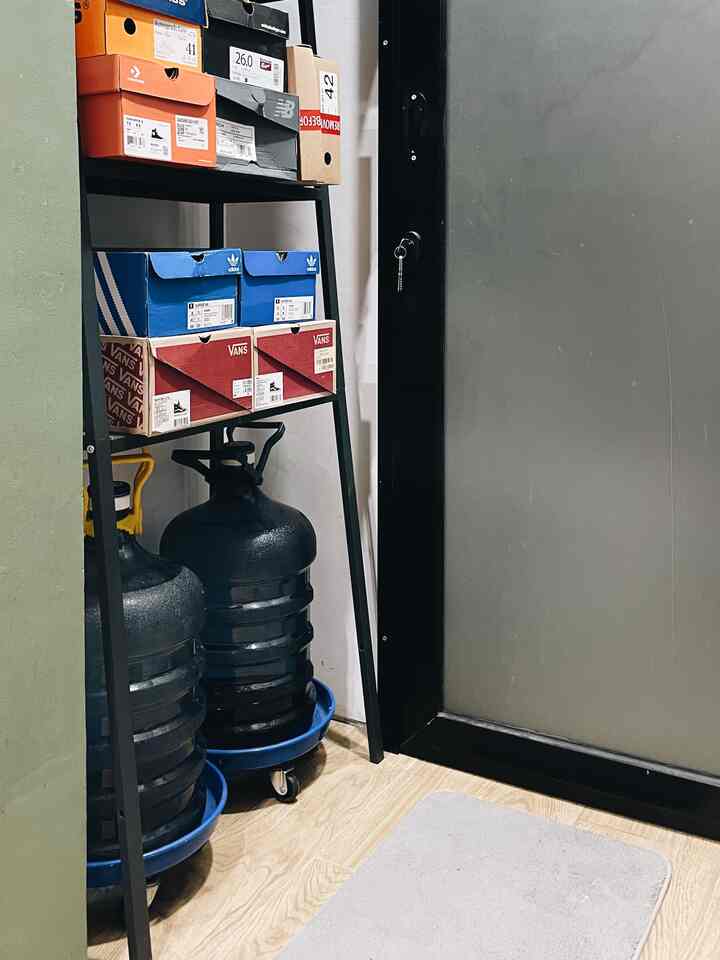 Narrow room corner featuring black metal shelving with shoe boxes and large water bottles on wood tone floor