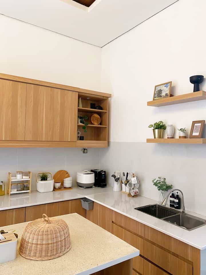 Natural-toned kitchen with wooden cabinets and white countertops, decorated with accessories and plants creating a cozy atmosphere