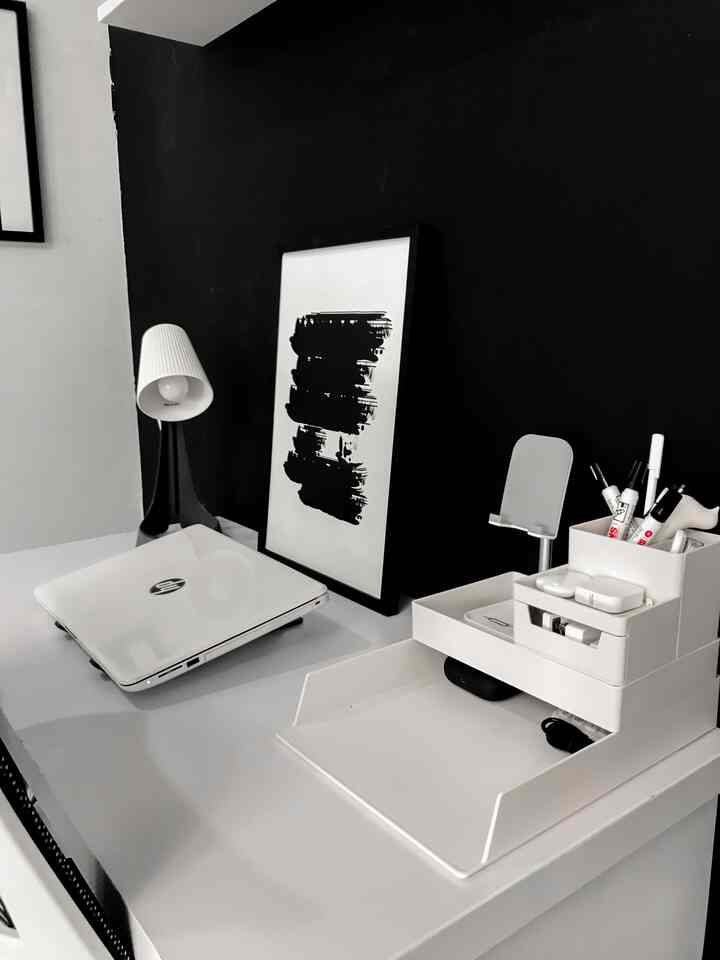 Monotone black and white home office space featuring a white desk with laptop and organizer, black wall with framed art creating a clean workspace