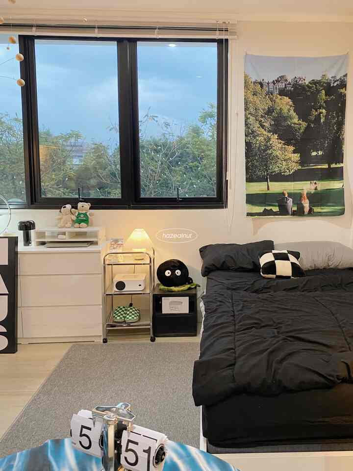 A bedroom featuring gray and black tones, with a landscape fabric poster on the wall, neat carpet and bedding creating a cozy atmosphere