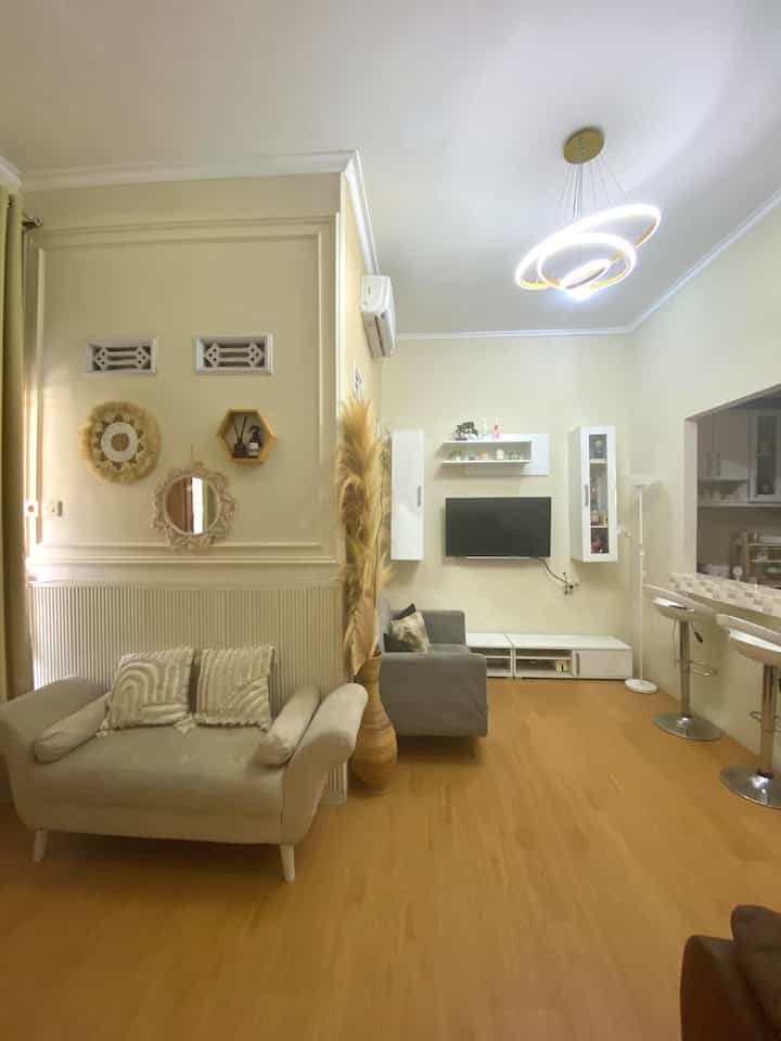 Cozy living room featuring gold pendant light and natural color wall moulding, beige sofas and TV cabinet arranged