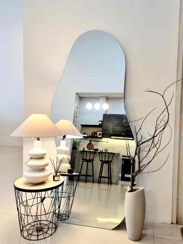 White and black toned kitchen space featuring a large curved mirror, floor lamp, and natural branch decor creating a cozy ambiance