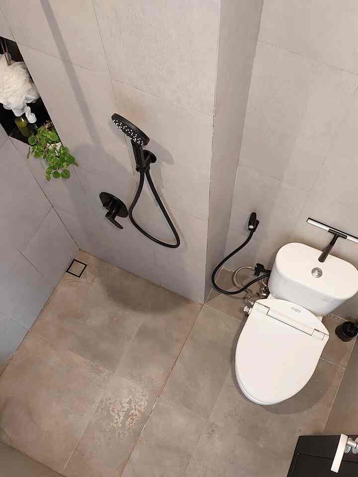 Gray-toned compact bathroom featuring a white toilet and black shower fixtures in a minimalist style home bathroom