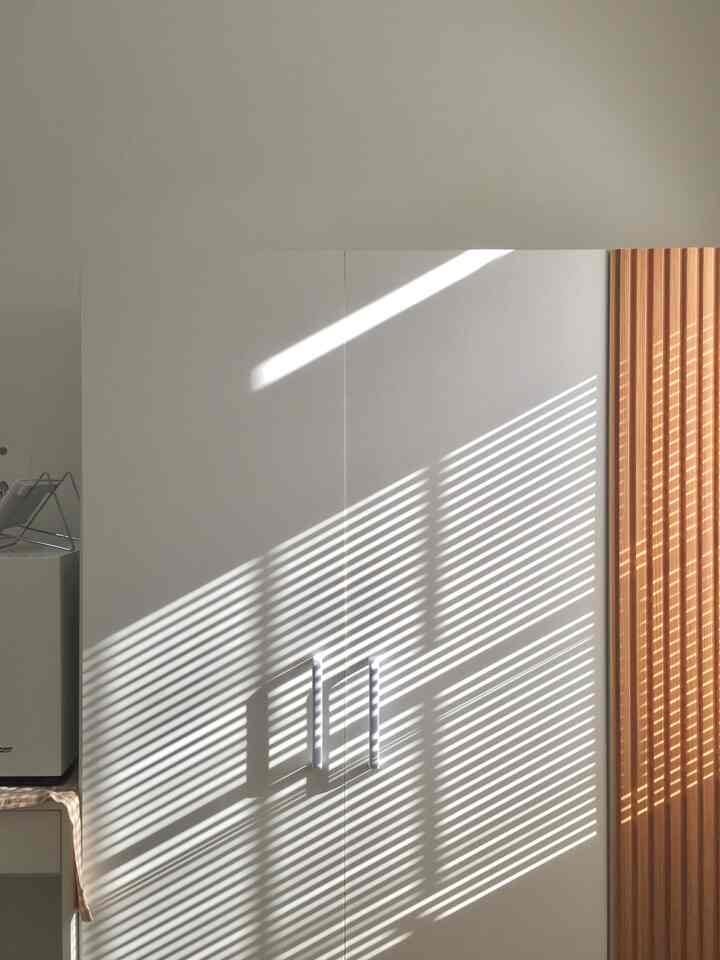 A clean bedroom featuring a white three-door wardrobe accented by warm wood tone wall panels with natural light shadows