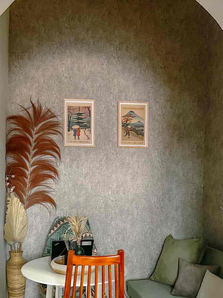 Mid-century modern living room featuring green sofa and brown wooden chair, Japanese print frames on textured wall creating cozy atmosphere