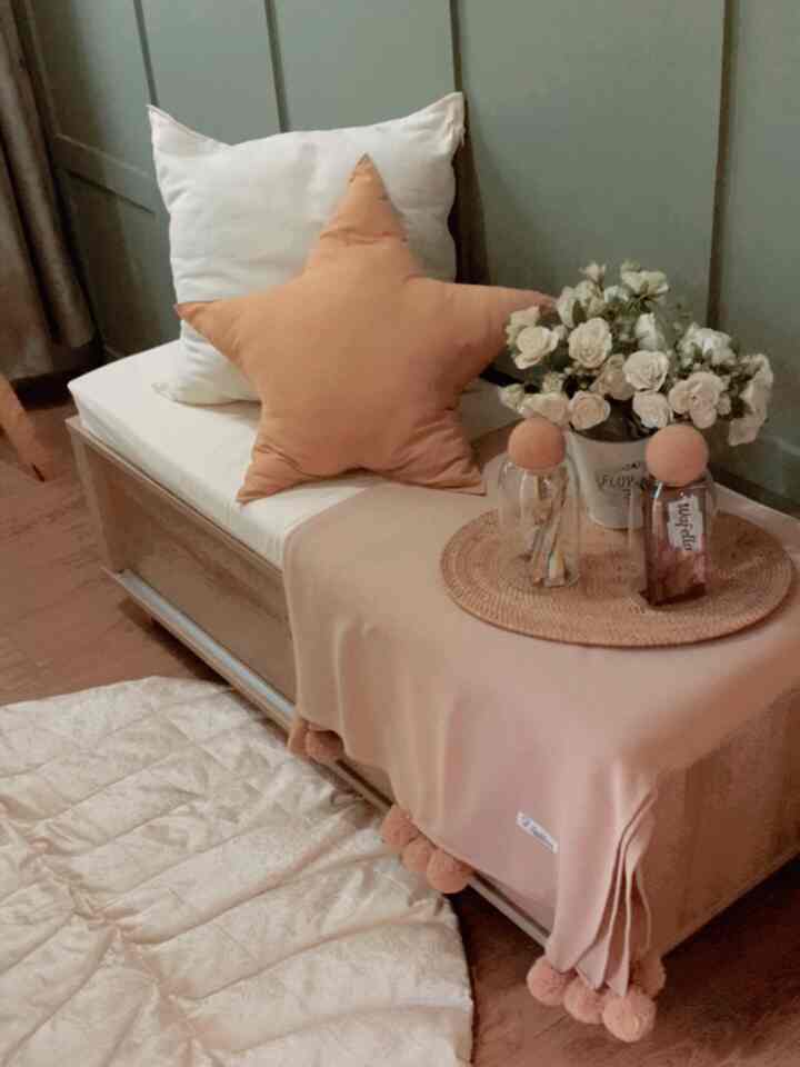 Beige and white toned small entrance area featuring star-shaped cushions, beige throw blanket, glass jars, and white roses creating a cozy atmosphere