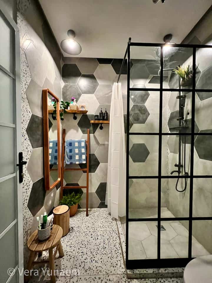 Gray and white toned bathroom featuring hexagonal tiles, black metal shower enclosure, and wood-tone accessories creating a modern look