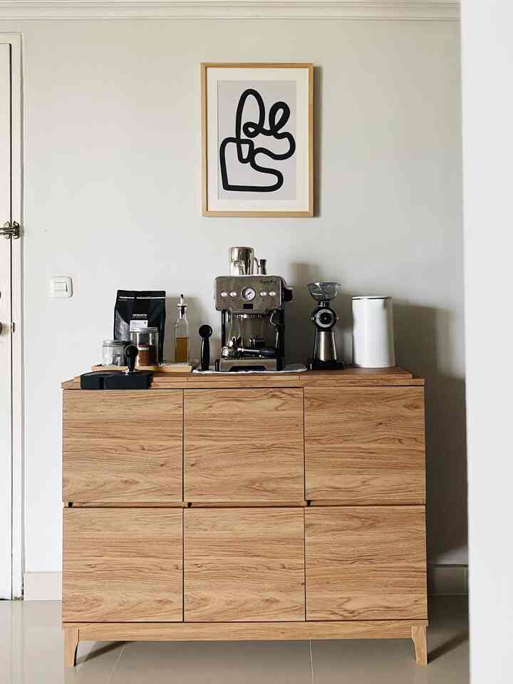 A minimalistic home cafe corner with white walls and wood tone cabinet, featuring a central espresso machine and grinder