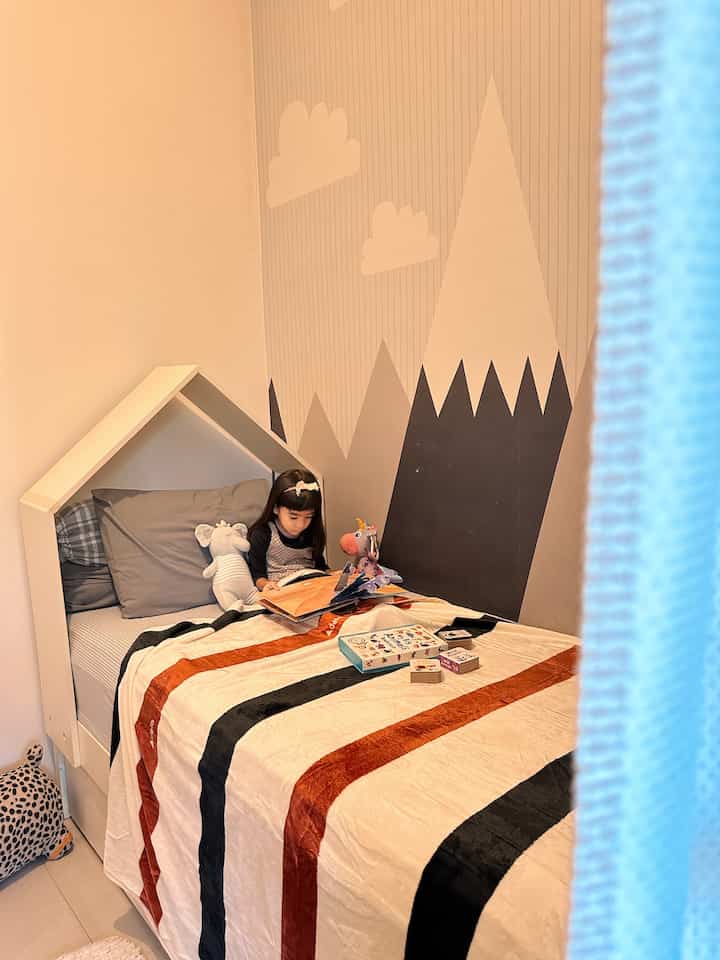 White and brown toned kids' room featuring a house-shaped bed and mountain-patterned wall mural with cozy atmosphere