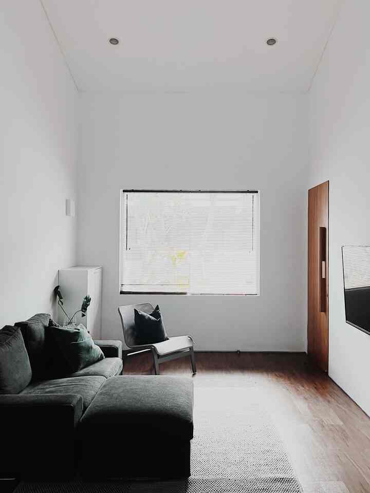 Minimal living room with dark gray sectional sofa, wood tone flooring, large window, and clean atmosphere