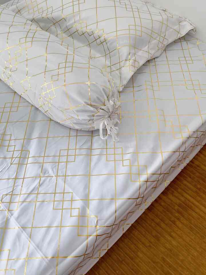Cozy bedroom featuring white bedding with gold geometric patterns and natural wood flooring