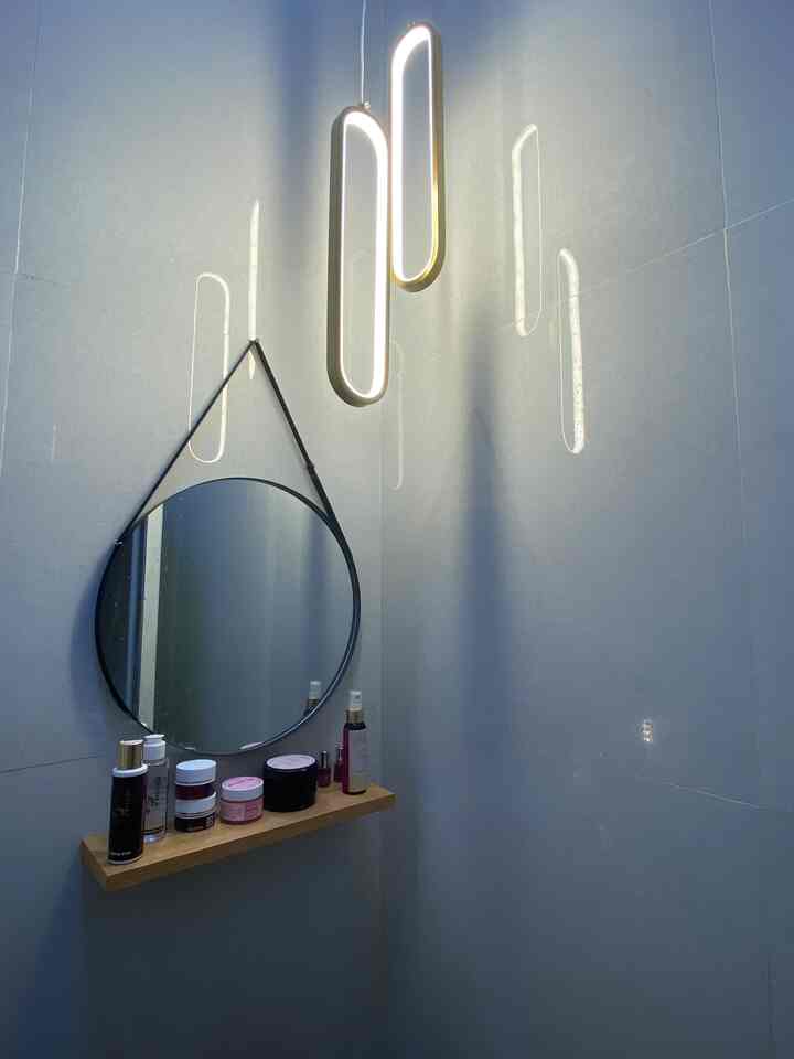 White-toned bathroom featuring a round mirror and cosmetics on a wooden shelf with modern pendant lighting in a simple space
