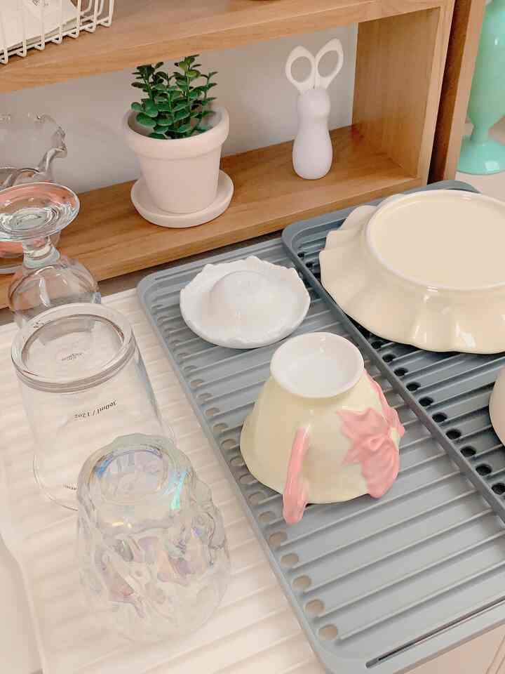 Bright and clean kitchen featuring a natural wood tone shelf and ivory walls, with cups and plates arranged on a dish rack