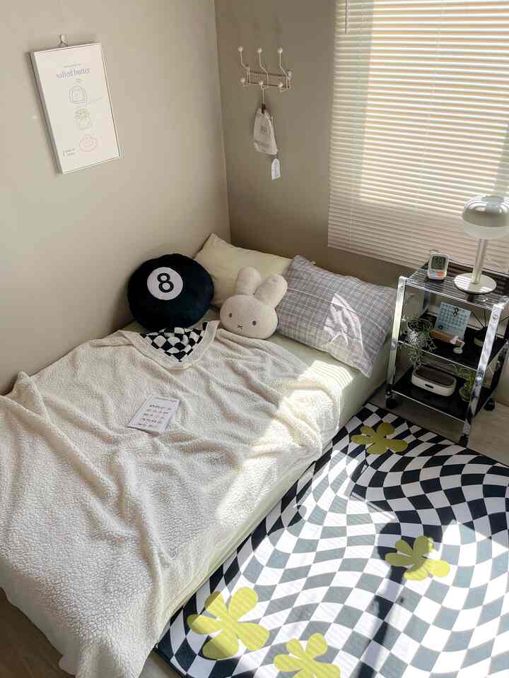 Bright ivory and white toned bedroom featuring bed with pillows and a fluffy blanket, shiny side table, and sunlit patterned carpet creating a cozy atmosphere