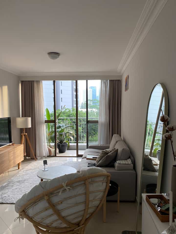 Natural modern toned living room featuring a light gray sofa, rattan chair, white walls, and sheer curtains with a cozy atmosphere