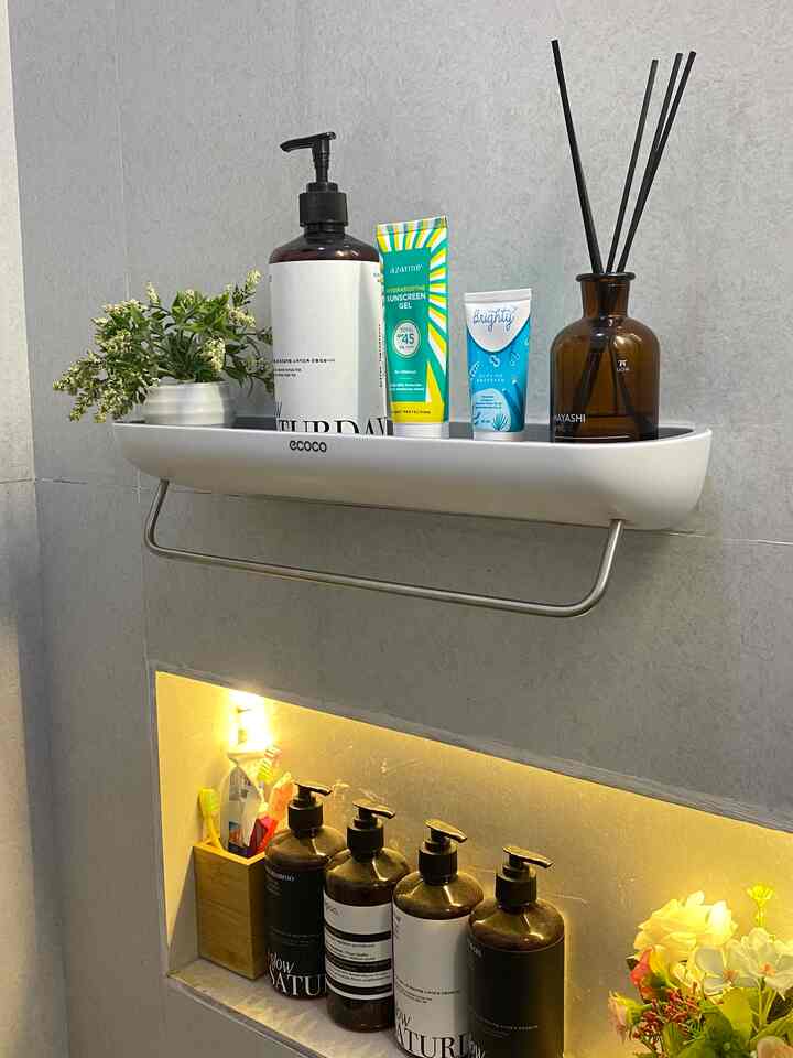 Gray-walled bathroom with a white shelf featuring diffuser and artificial flowers, creating a natural and tidy atmosphere