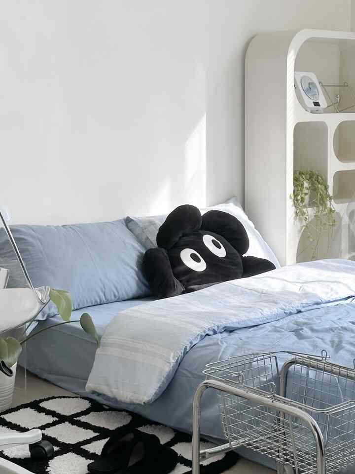White-toned bedroom with simple design featuring blue bedding, a black cushion, and patterned carpet in a clean space