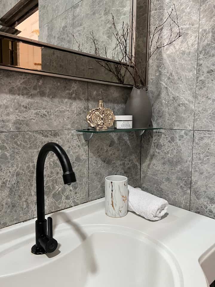 Modern bathroom space with gray marble tiled walls, black faucet, and white washbasin