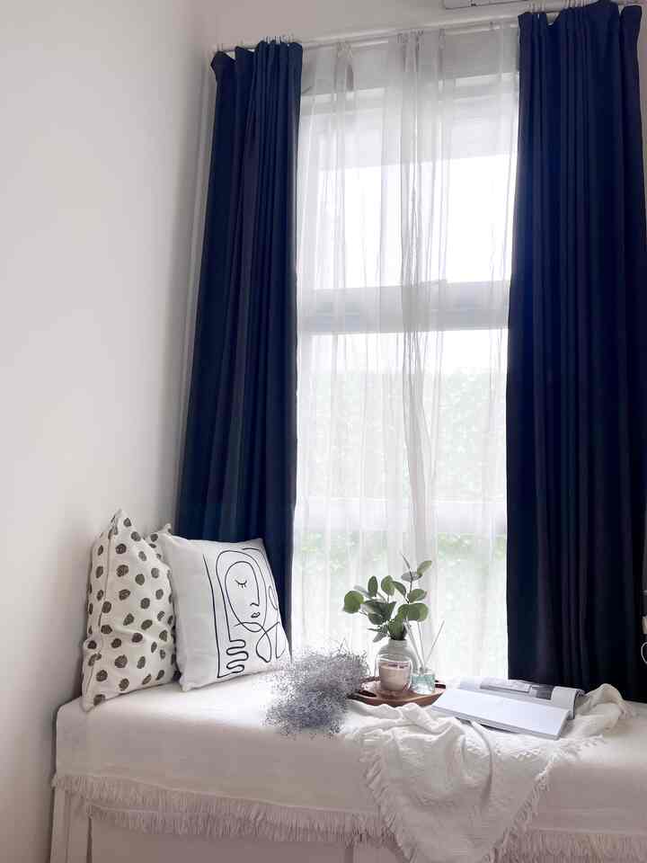 Bright white-toned bedroom space featuring navy curtains and cushions, with a simple and natural interior