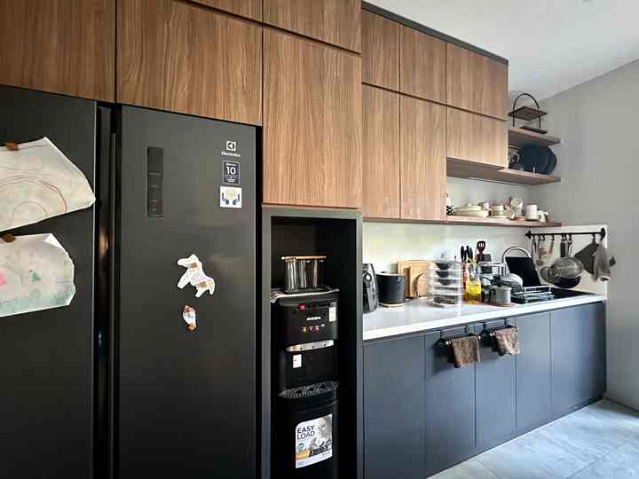 Modern kitchen featuring brown wood-tone cabinetry and black refrigerator with organized kitchen utensils