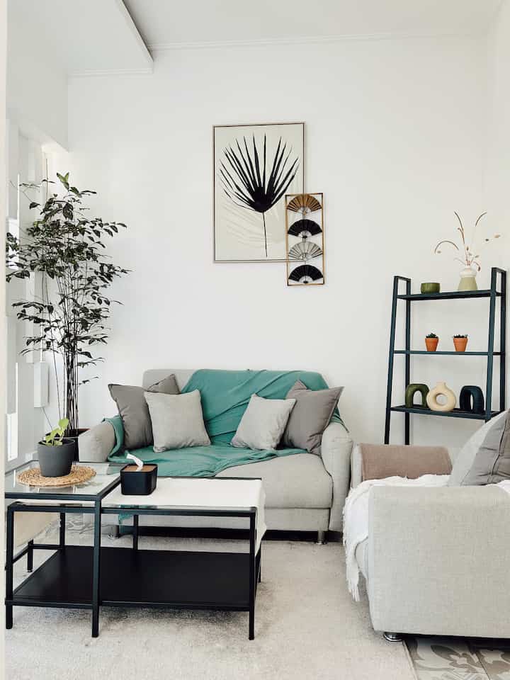 Natural-toned living room with gray sofas and white walls, featuring plants and shelving for storage in a clean layout