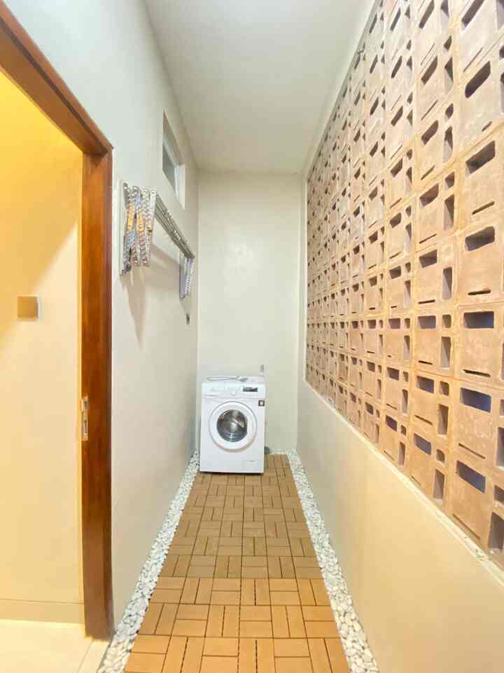 Narrow long balcony with white walls and brown roster brick wall, featuring washing machine and foldable drying rack in a practical laundry area