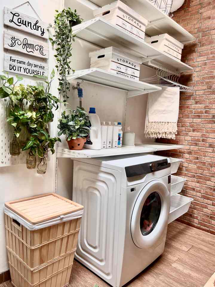 White and natural-toned compact long laundry room featuring storage shelves, plants, and wooden laundry basket with clean atmosphere