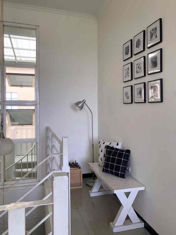 White-toned narrow corner space featuring a bench, floor lamp, and book box; simple and cozy reading nook