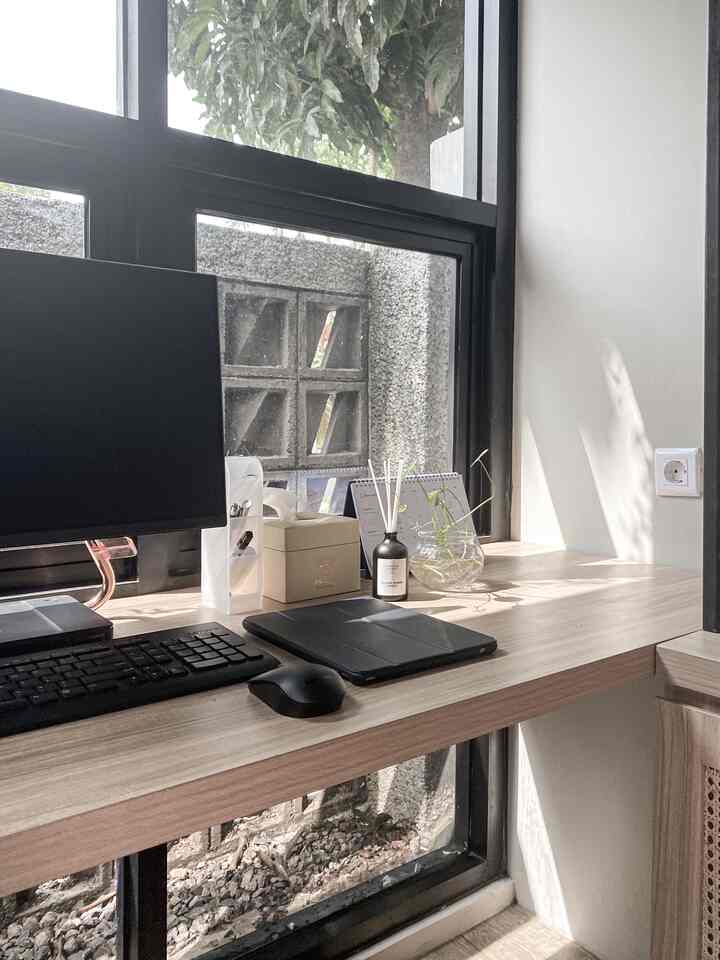 Natural-toned home office space featuring a large desk with a monitor, plants, and transparent glass vases arranged neatly in a bright work area