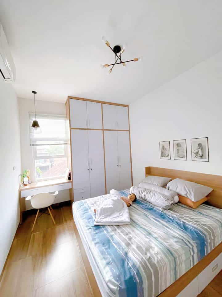 Japandi-style bedroom with white walls and wood-tone furniture, featuring a baby lying on the bed