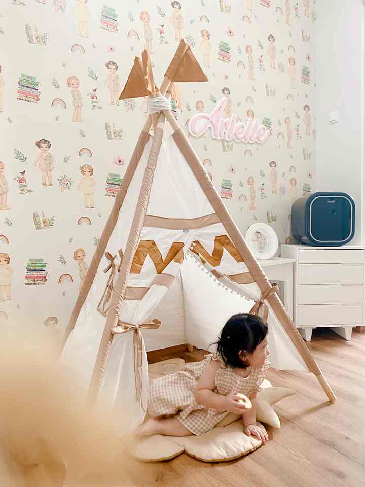 Natural-toned kids' room featuring beige and white teepee tent with child seated on wooden floor mat, cozy play area