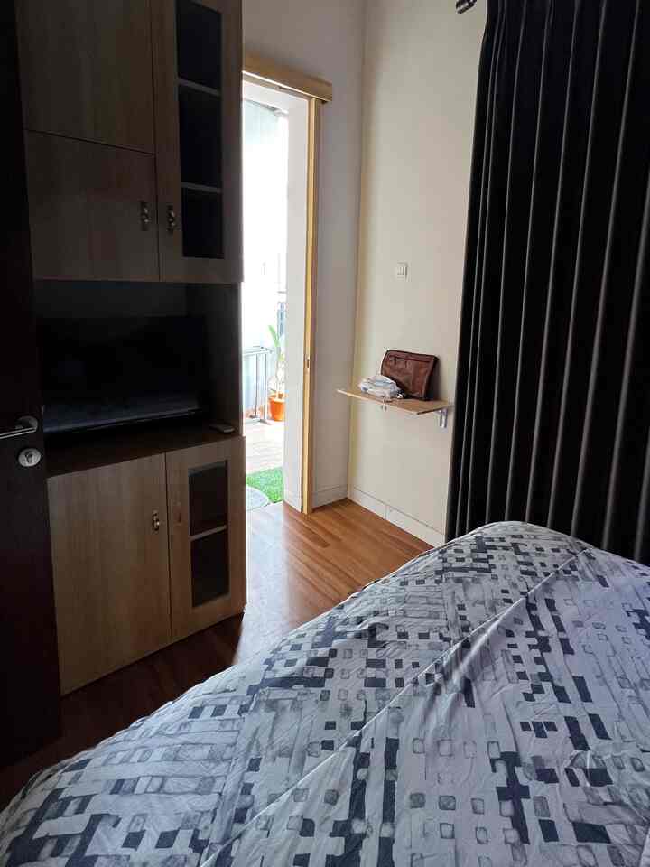 A natural-tone compact bedroom with white walls, wood flooring, patterned bedspread, and a wall-mounted foldable table creating a cozy atmosphere