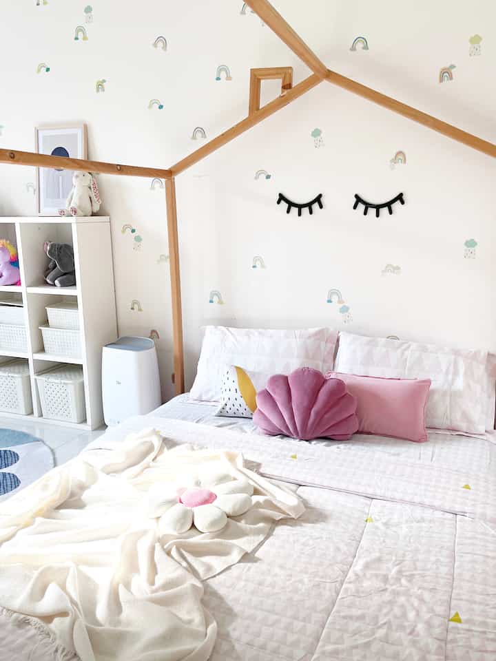 Bright white and pink toned kids' room featuring wooden bed frame and toy storage shelves with cozy, cheerful atmosphere