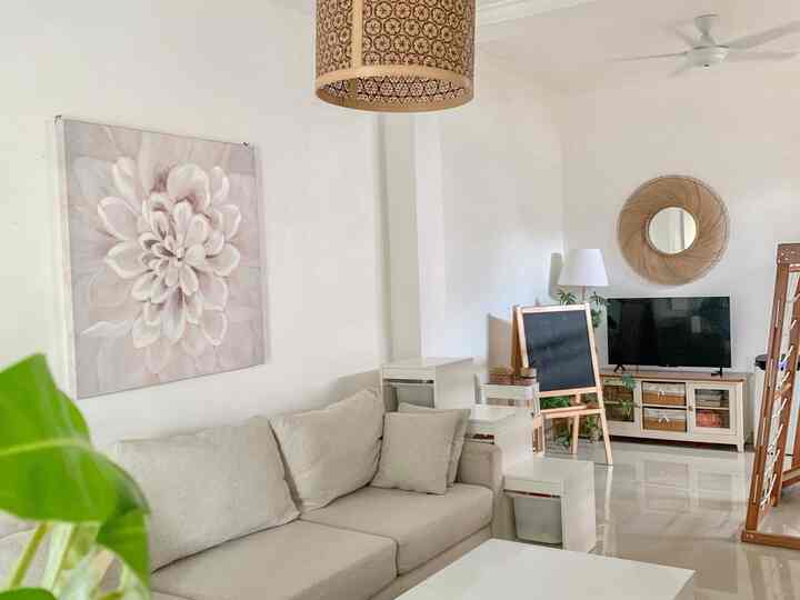 A bright and beige-toned compact living room featuring a beige sofa, plants, and a round wall mirror, creating a natural and minimalist atmosphere
