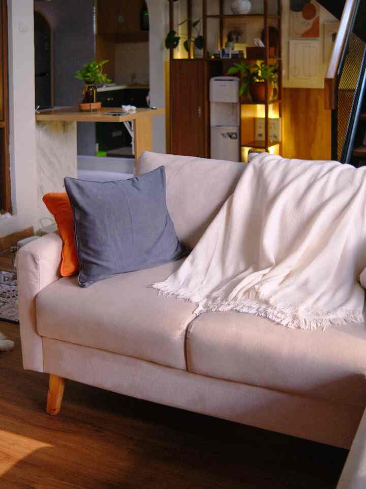 Warm beige and wood tone living room featuring beige sofa with gray and orange cushions and a white blanket for cozy atmosphere