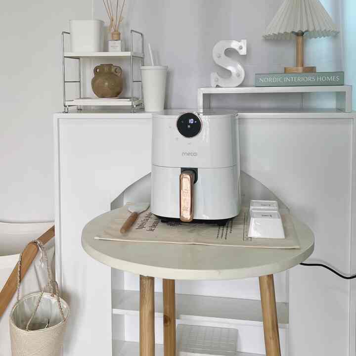 A clean and simple kitchen space with white and wood tones, featuring an air fryer and round table centrally placed