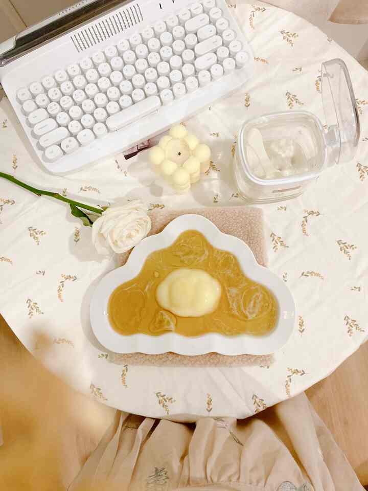 White and beige toned kitchen table featuring cloud-shaped plate, candle, and flower creating a cozy setting
