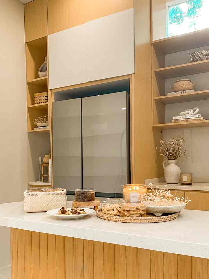 Natural toned kitchen space with wooden cabinetry and bright kitchen island featuring snacks and floral decor, creating a cozy atmosphere