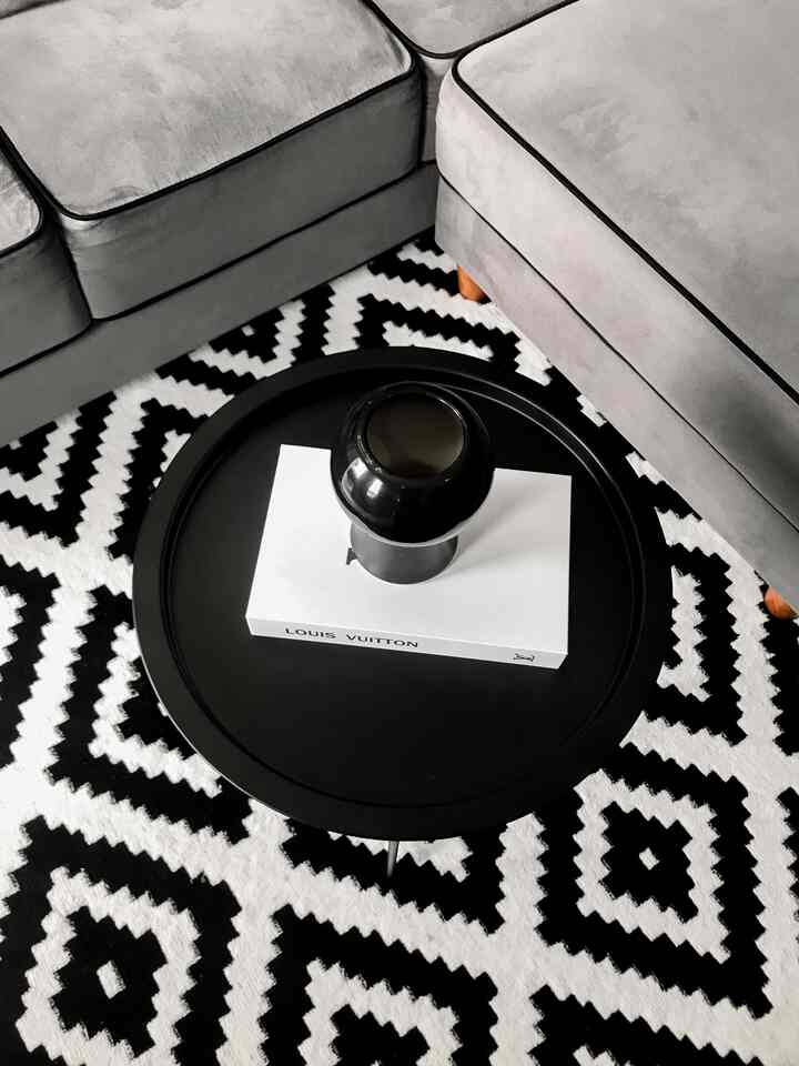 Monotone living room featuring gray sectional sofa, black and white zigzag carpet, and round coffee table with simple modern vibe